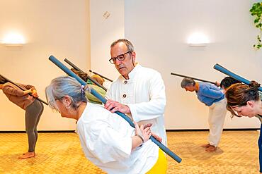 Qi gong class members using tube to stretch the back with the guidance of a male instructor