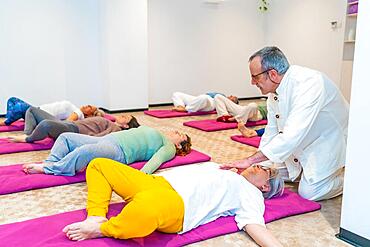 Instructor leading a breathing exercise in a Qi gong class with several women lying on mats on the floor