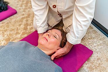 Qi gong teacher massaging the neck of a woman while meditating and breathing on the floor