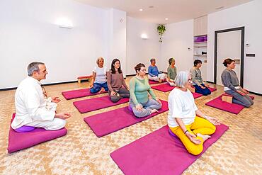 Yoga class full of mature caucasian women doing lotus position and meditating