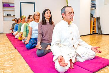 Yoga teacher leading a meditation in a community sitting on mat with lotus position