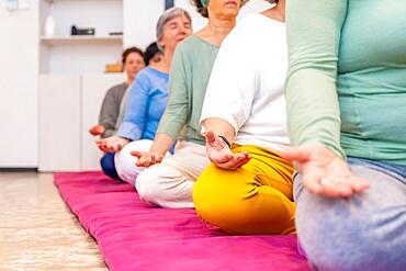 Cropped photo with copy space on left of part of people meditating on a mat in lotus position