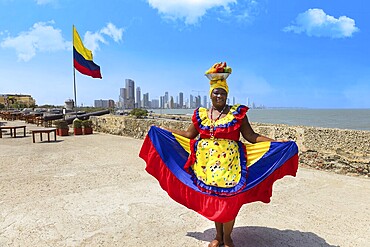 Cartagena, Colombia, 8 May, 2024: Colombia, lady in national colorful costume posing in Walled City historic center of Cartagena near Colombian flag, South America