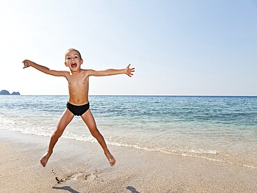 Summer vacations, little smiling child boy jumping on sea sand beach