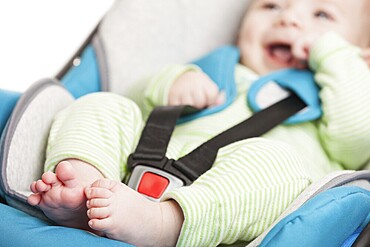 Little smiling baby child fastened with security belt in safety car seat