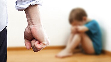 Family violence and aggression concept, furious angry man raised punishment fist over scared or terrified child boy sitting at wall corner