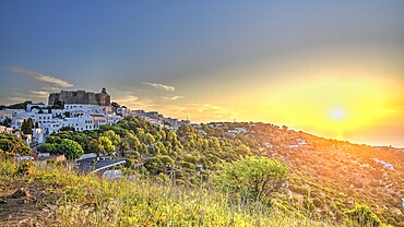 View of a castle and a white village on a hill at sunset, surrounded by green nature, Chora, main town of Patmos, Patmos, Old Town, Dodecanese, Greek Islands, Greece, Europe