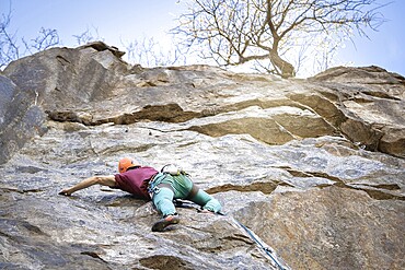 A man climbs a rugged rock face in nature, embracing the thrill of extreme sports. His determination and skill are evident as he ascends, showcasing the adventure and challenges of rock climbing