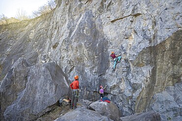 Three climbers with backpacks ascend a rocky mountain trail, showing their adventurous spirit and determination. One of them is wearing an orange helmet, emphasizing safety. This image captures the essence of outdoor exploration and mountaineering