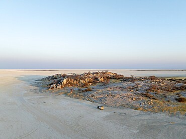 Rocky island with baobab trees in a dry salt pan, at sunset, off-road vehicle on the salt pan, aerial view, Kubu Island, Botswana, Africa