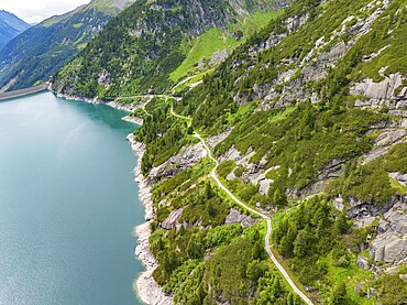 The shoreline of a reservoir with a road winding along the mountains, under a cloudy sky, Klein Tibet, Zillertal, Austria, Europe