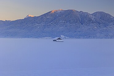 Hut in the snow in front of mountains, evening light, view of Rabenkopf and Benediktenwand, Schlehdorf, Alpine foothills, Upper Bavaria, Bavaria, Germany, Europe