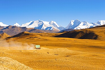 A truck drives through the barren landscape of the mountainous border between Tibet and Nepal as snowcapped himalayan mountain peaks poke through in the distance