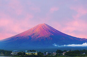 Fiery colorful sky above the red crater cone of Mount Fuji at dawn sunrise over Lake Kawaguchiko water on a summer morning in Japan