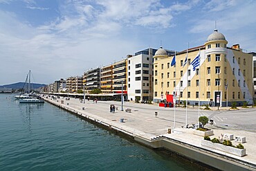 Harbour promenade next to calm water with sailing boat and people along the picturesque buildings, on the right Papastratos tobacco warehouse building, heritage building, Argonafton street, Volos, Pagasitic Gulf, Thessaly region, Greece, Europe