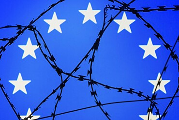 Symbolic image, migration, defence against refugees wanting to enter the EU, barbed wire overarches the stars of the EU flag against a blue sky, border, border fence