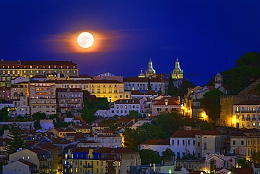 Beautiful view of big full moon over Lisbon areas of Sao Vincente de Fora church, Sao Jorge castle and houses downhill, Portugal. Supermoon, close up, Europe, night, landscape, cityscape, clear sky. Romantic evening, fairy tales, stories