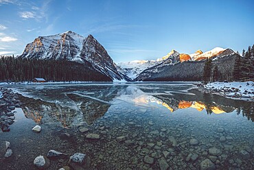 Peaceful lake reflecting snow-capped mountains and a cabin under a clear blue sky at sunrise, Lake Louise, Canadian Rockies