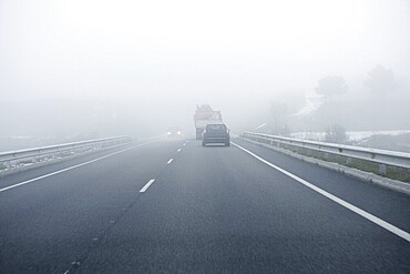 Foggy gray road, cars driving fading into the fog