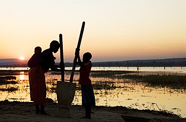 Tonga women at sunset, pounding grain at the shore of Lake Kariba, Zambia, Africa