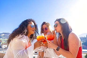 Women enjoying summer during a party drinking cocktails together with straw in a roof terrace