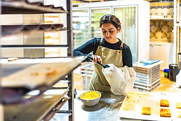 Female latin artisan baker filling a piping bag to decorate pastries in the workshop kitchen of a bakery