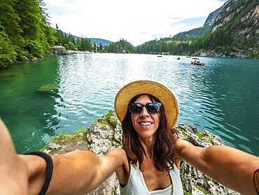 Young woman taking selfie at lake braies with rowboats in the background, enjoying summer holidays in the dolomites