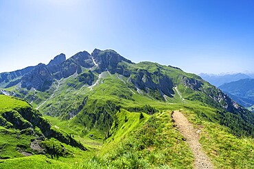 Scenic view of a hiking path leading through vibrant green mountains under a clear blue sky in the italian dolomites