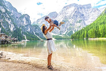 Tourist mother lifting her son in the air while enjoying summer holidays at lake braies, also called pragser wildsee, in the dolomites of italy
