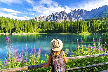 Female tourist admiring the stunning turquoise waters of lake carezza with the latemar mountain range in the background, dolomites, italy