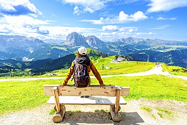 Hiker relaxing on a bench and admiring the odle mountains in val di funes, south tyrol, italy