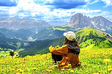 Woman hiker sitting in a vibrant flower field, admiring the stunning seceda peaks rising majestically in the dolomites of italy