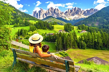 Mother and son enjoying a relaxing moment on a bench, admiring the breathtaking panorama of the odle mountains in val di funes, dolomites, italy