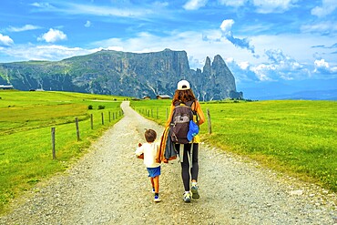 Mother and son walking on a gravel road at alpe di siusi, enjoying summer vacation in the dolomites