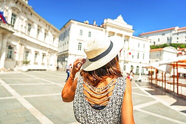 Tourist holding her straw hat while visiting tartini square in piran, slovenia, during a sunny summer day