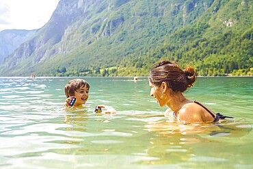 Mother and son enjoying summer fun, playing with toys while swimming in the refreshing waters of lake bohinj, surrounded by the julian alps