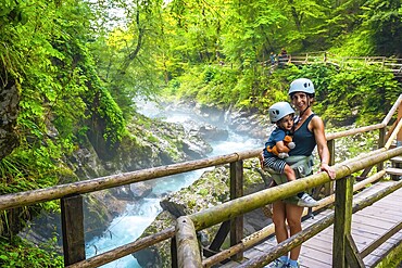 Mother carrying her child while visiting the stunning vintgar gorge near bled, slovenia, enjoying a breathtaking view of the turquoise river and lush forest