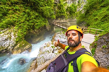 Tourist wearing helmet and backpack hiking in vintgar gorge, near bled, slovenia, making thumbs up sign by the radovna river