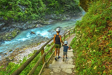 Tourists wearing helmets are enjoying a summer walk along the stunning turquoise radovna river flowing through the vintgar gorge near bled, slovenia
