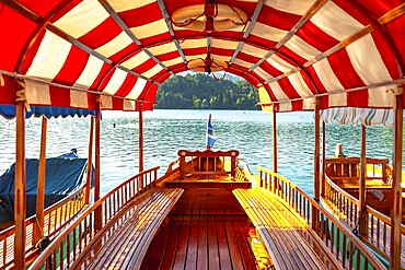 Wooden tourist boat with red and white canopy sailing on lake bled in slovenia, offering scenic view of bled island