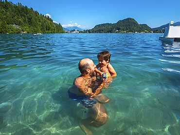 Father and son having fun swimming in the clear waters of lake bled, surrounded by the beauty of the julian alps in slovenia