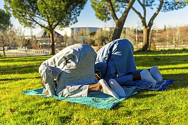 Two african muslim men are kneeling in prayer on prayer rugs in a park, wearing traditional clothing