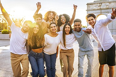 Portrait of diverse group of cheerful young people having fun and raising arms while standing through the city