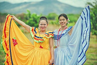 Portrait of two Hispanic women wearing cultural folkloric costume in a field. Two smiling Hispanic girls wearing cultural folkloric costumes outdoors