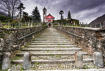 long stairs leading up to an old rose colored church under an expressive overcast sky in the Maggia Valley in Switzerland