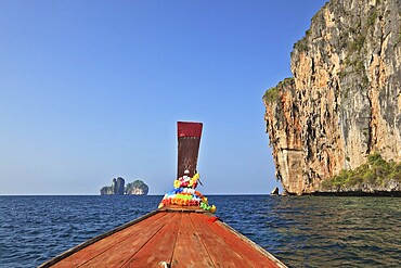 The Thai excursion boat floats to ocean island. The boat nose is decorated by multi-colored and bright silk scarfs