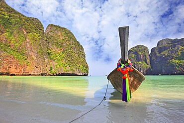Scenic green islands of Thailand coast. Emerald sea and fine white sand. On the beach approached by a native boat for tourists, decorated with a red silk scarf