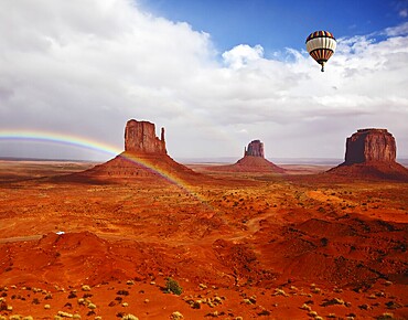 Huge balloon flies over Red Desert Navajo, USA. The picturesque rainbow crosses some rocks - mittens. On the road is a white jeep