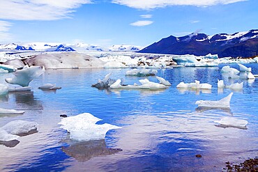 Cold, clear July day. Bizarre icebergs and floating ice floes reflected in the smooth cold water of the lagoon. The lagoon Jokulsaurloun. Iceland. The concept of eco, northern and photo tourism