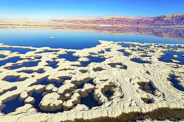Dead Sea. Evaporated salt forms bizarre patterns on the water. Sunny winter day. The blue water is surrounded by pink mountains. The picture was taken by a drone from a aerial view. Israel